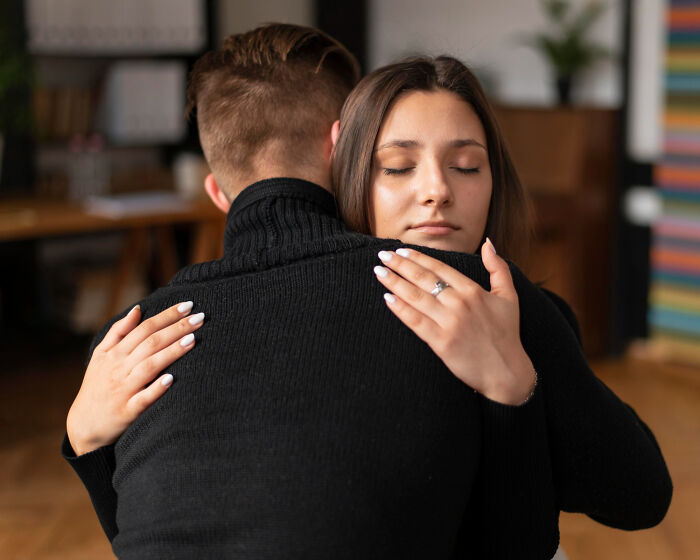Young woman with closed eyes hugging a man, reflecting small signs of a challenging childhood experience.