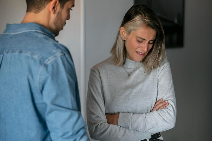 A woman looking distressed with arms crossed while a man in a denim shirt talks, showing signs of troubled childhood.