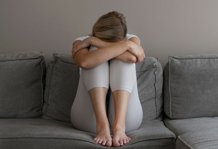 Person sitting on a gray couch with head buried in arms, showing emotional struggle related to committed lies.