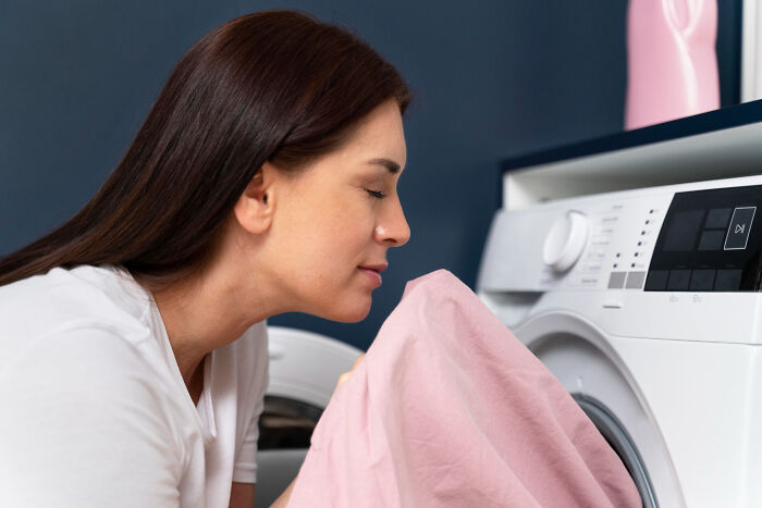 Woman smelling freshly washed laundry near washing machine, illustrating habits related to bite my nails including toenails.