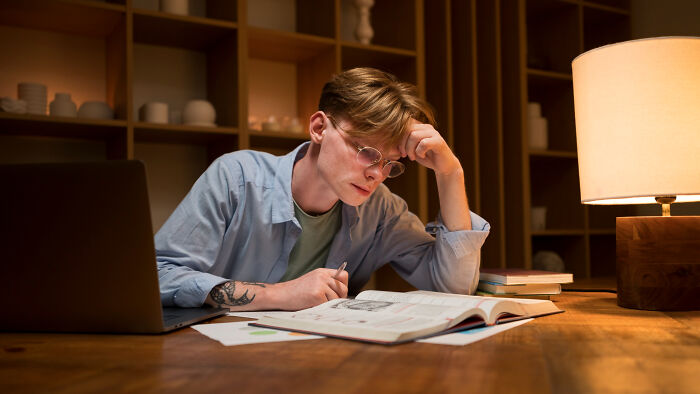 Young man intensely studying at night, showing commitment to a lie with focused expression and open books nearby.