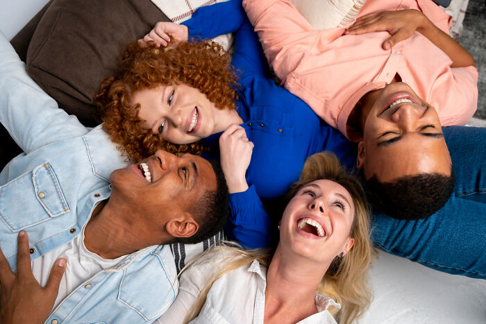 Four friends lying on a couch smiling and laughing together in a casual setting, showing completely legal total psychopath energy.