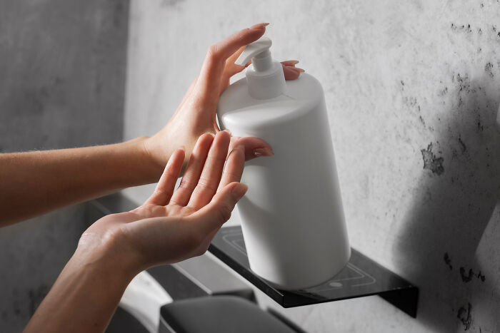 Person dispensing lotion from a white pump bottle against a gray concrete wall, illustrating poor people habits.