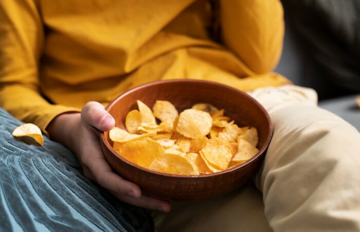 Person wearing yellow shirt holding a bowl of potato chips, illustrating things non-Americans do like breaking spaghetti in front of Italians