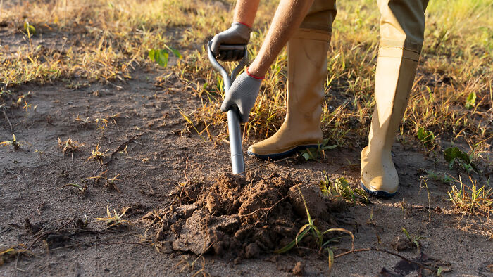 Person wearing gloves and rubber boots digging soil outdoors, representing completely legal total psychopath concept.