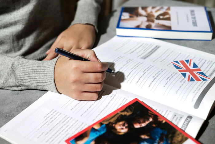 Person writing notes in a workbook with a UK flag card nearby, illustrating UK perspectives and opinions.