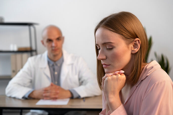 Woman looking frustrated and dismissed during a medical consultation with a doctor in a clinical setting.