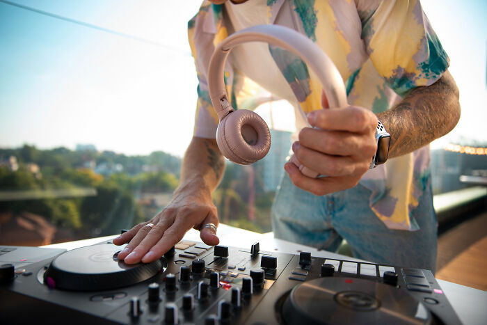 DJ holding wireless headphones while using a mixer at an outdoor event, capturing a bar safe word atmosphere.