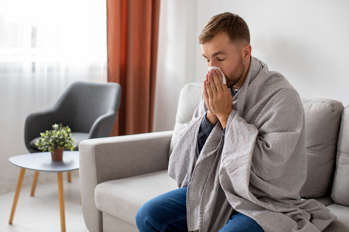 Young man wrapped in blanket sitting on couch, showing small signs that indicate childhood might not have been all rainbows and ponies.