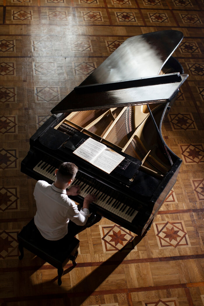 Man playing a grand piano on an ornate wooden floor, showcasing the lifestyle of out-of-touch rich people flaunting wealth.
