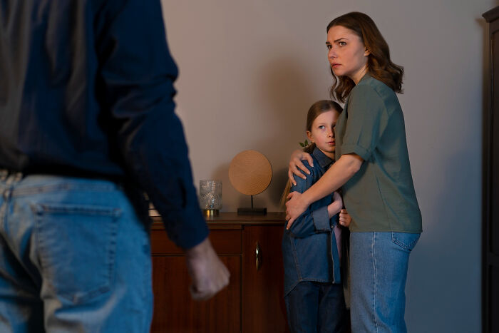 Woman protectively hugging her child while facing an angry person, showing signs of a difficult childhood experience.