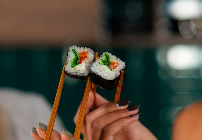 Two hands holding sushi rolls with chopsticks, highlighting people committed to a lie way too hard moment.