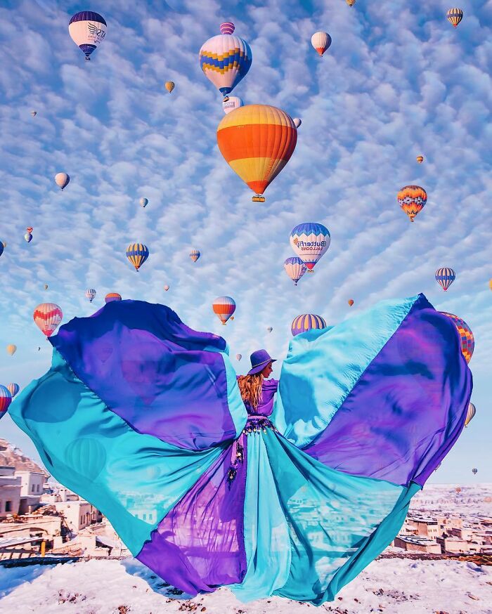 Woman in flowing blue and purple dress among colorful hot air balloons, showcasing breathtaking travel photos and scenic adventure.