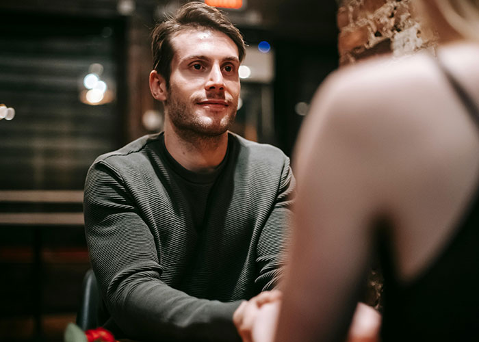 Man and woman on an awkward date at a restaurant, with tense expressions and waitstaff in the background.