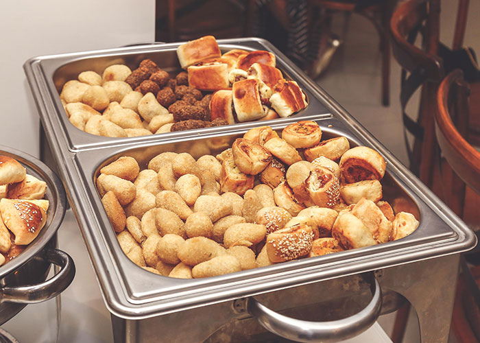 Assorted baked goods displayed in metal trays at a buffet, showcasing a variety of pastries and rolls.
