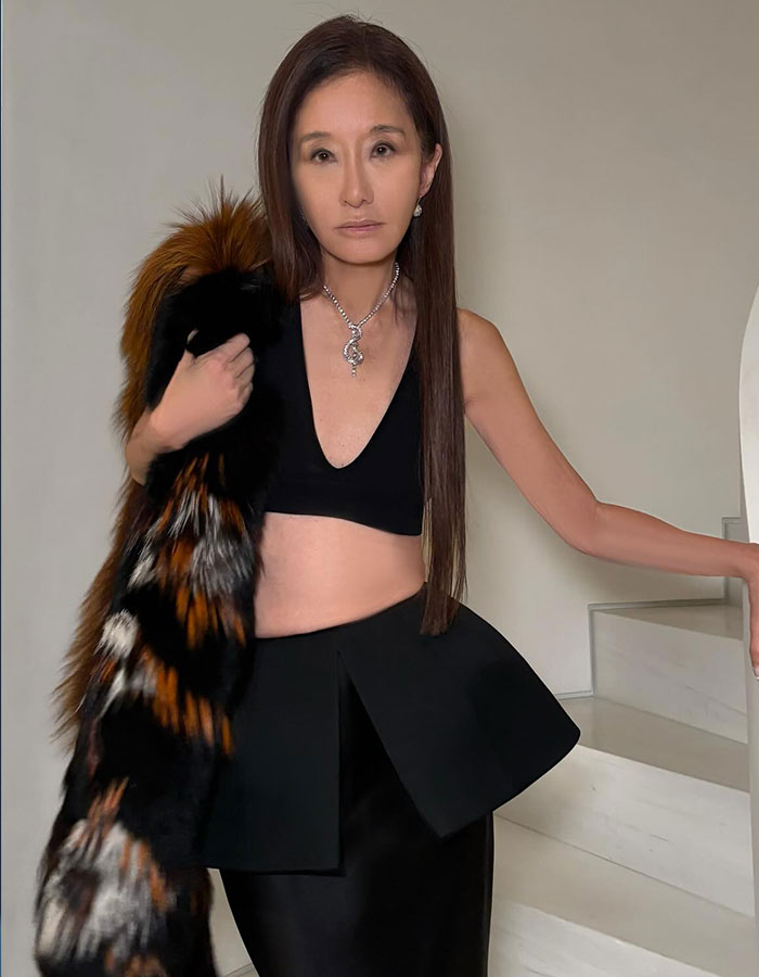 Asian celebrity posing indoors wearing a black outfit and fur stole, showcasing a look way younger than actual age.