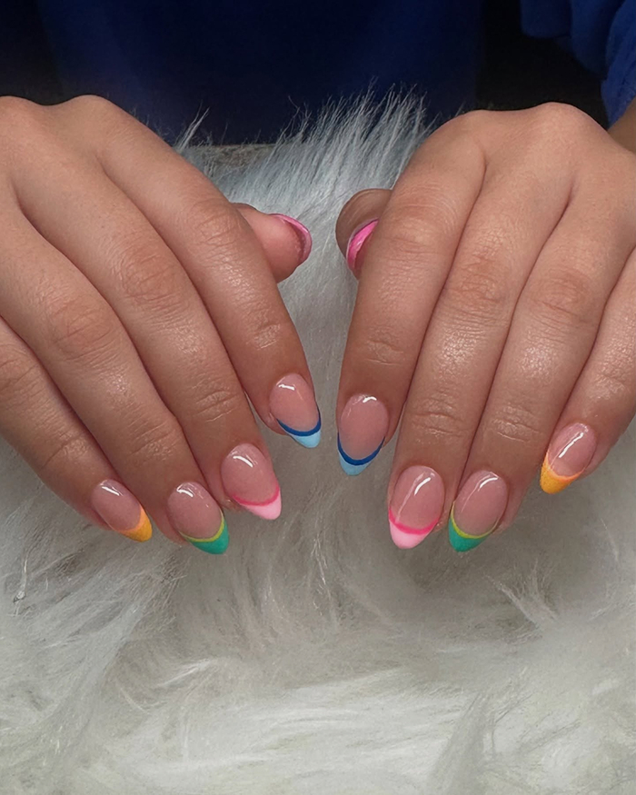 Hands displaying colorful French tip nails with bright summer-inspired shades on a soft white fur background, summer nails trend.