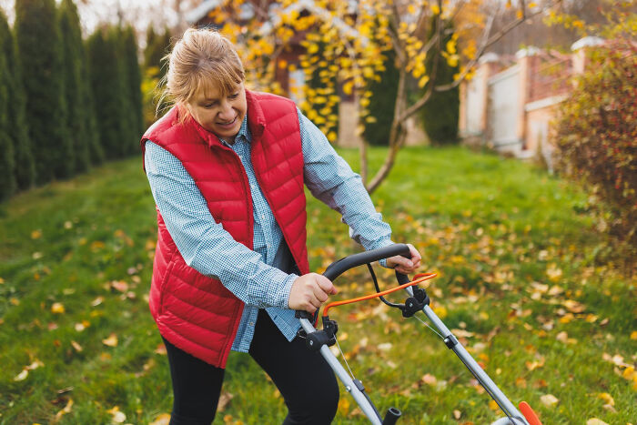 Woman committed to a lie way too hard while pushing a lawn mower in a backyard with autumn leaves.