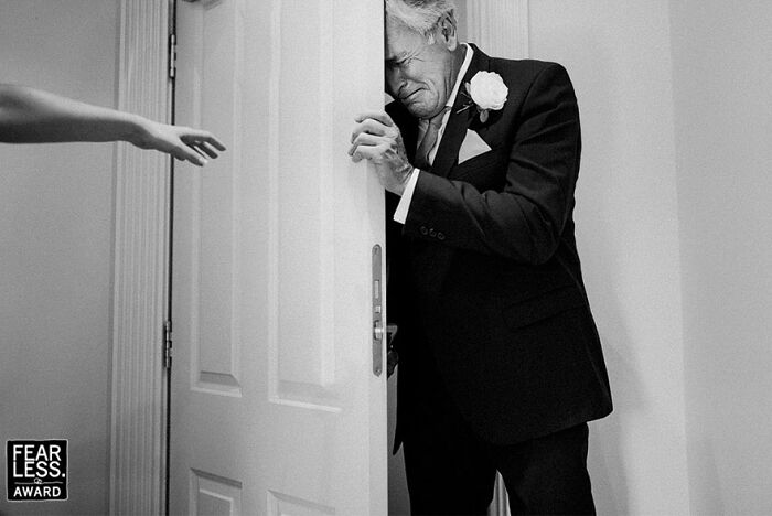 Emotional groom hides behind door as bride reaches out during unforgettable wedding photo shared by community.