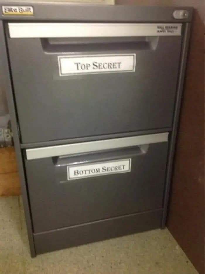 Gray filing cabinet with humorous labels top secret and bottom secret, a funny work meme to keep you going at the office.