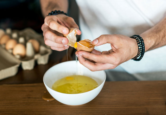 Hands cracking an egg into a bowl, illustrating old wives tales and traditional home remedies in the kitchen.