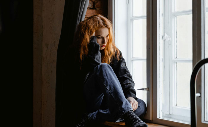 Young woman with red hair sitting by a window, deep in thought, reflecting on therapy revelations and emotional insights.