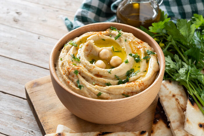 Bowl of creamy hummus garnished with olive oil, chickpeas, and parsley, a healthy best processed foods weight loss option.