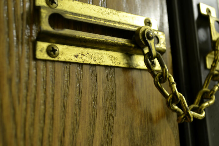Close-up of a vintage brass security chain lock on a wooden door, symbolizing unresolved personal mysteries.