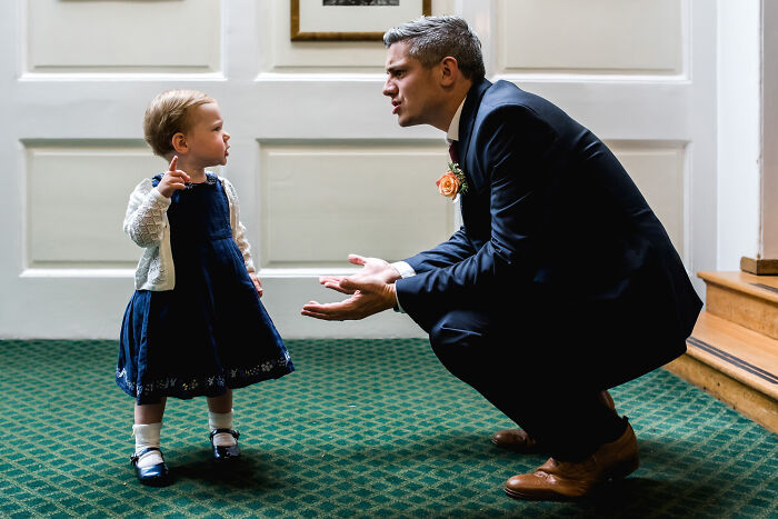 Man in suit crouching to talk to toddler girl in dress and cardigan in an unforgettable wedding photo shared by community