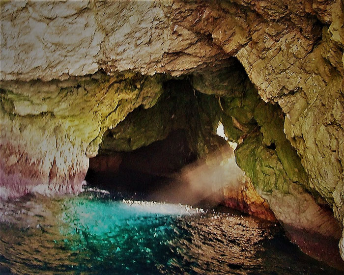 Sunlight shining into a rocky cave with turquoise water inside one of the scariest places around the world for brave travelers