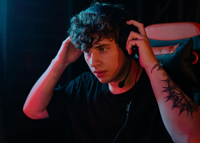 Young man with headset adjusting microphone, focused during a gaming session, showing a team moment sacrifice expression.