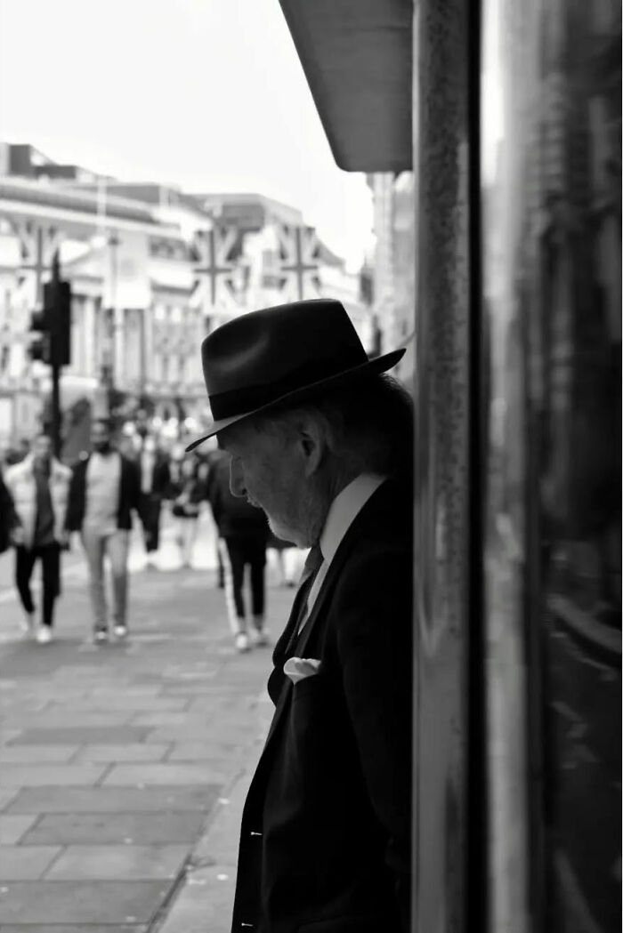 Black and white street shot of an elderly man in a hat and suit, capturing the poetry of everyday life in the city.