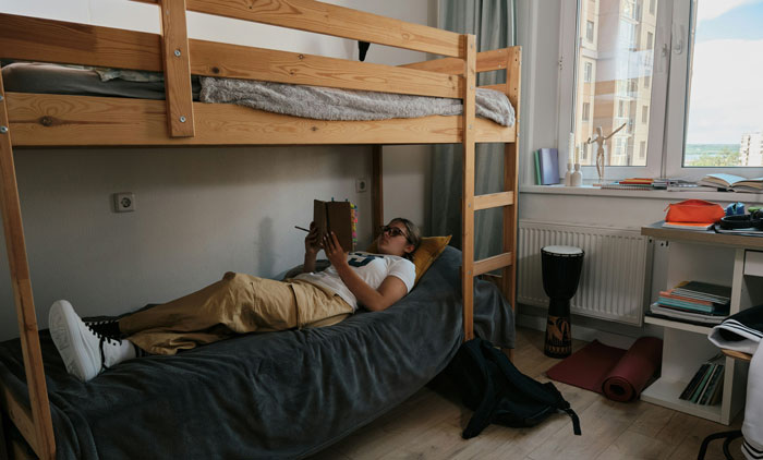 Person reading a book on a bunk bed, reflecting on the biggest mistake of their life in a cozy bedroom setting.