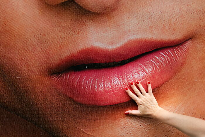 Close-up of a hand with red nails touching a large street photo of lips, showcasing perfectly-timed street photography.