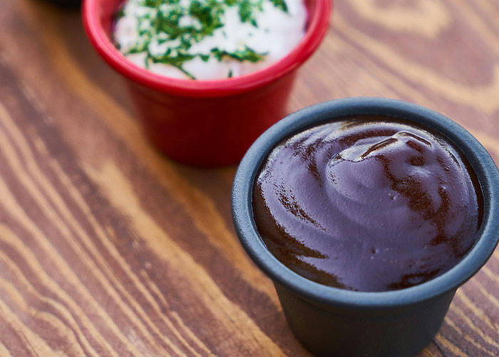 Close-up of barbecue sauce and ranch dip in small containers on a wooden table, related to buffet workers encounters.