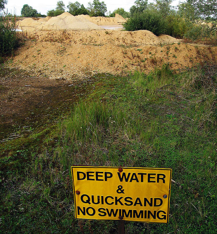 Warning sign saying deep water and quicksand with no swimming near a sandy area, relating to biggest lies millennials were told.