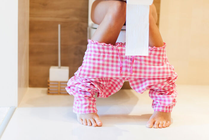 Person sitting on a toilet with pink checkered pants down, related to pregnancy, childbirth, and postpartum facts.