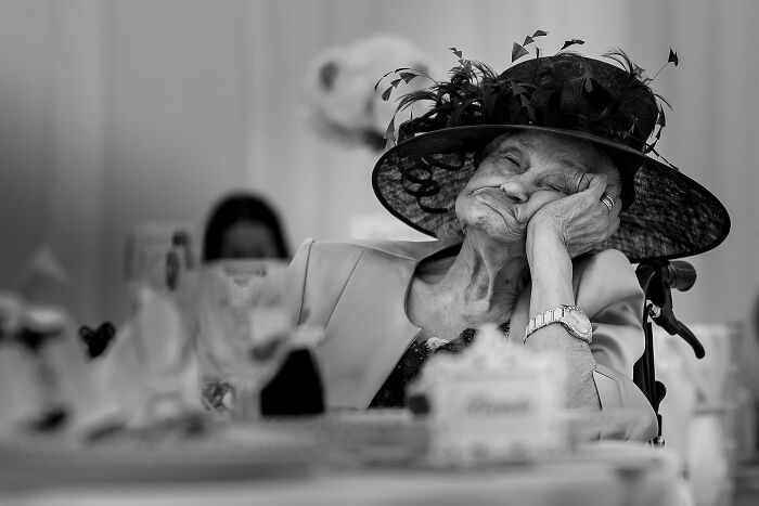 Elderly woman in an elegant hat resting her head on hand captured in an unforgettable wedding photo.
