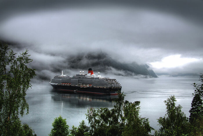 Cruise ship sailing through misty fjords surrounded by lush green trees in breathtaking travel photos.