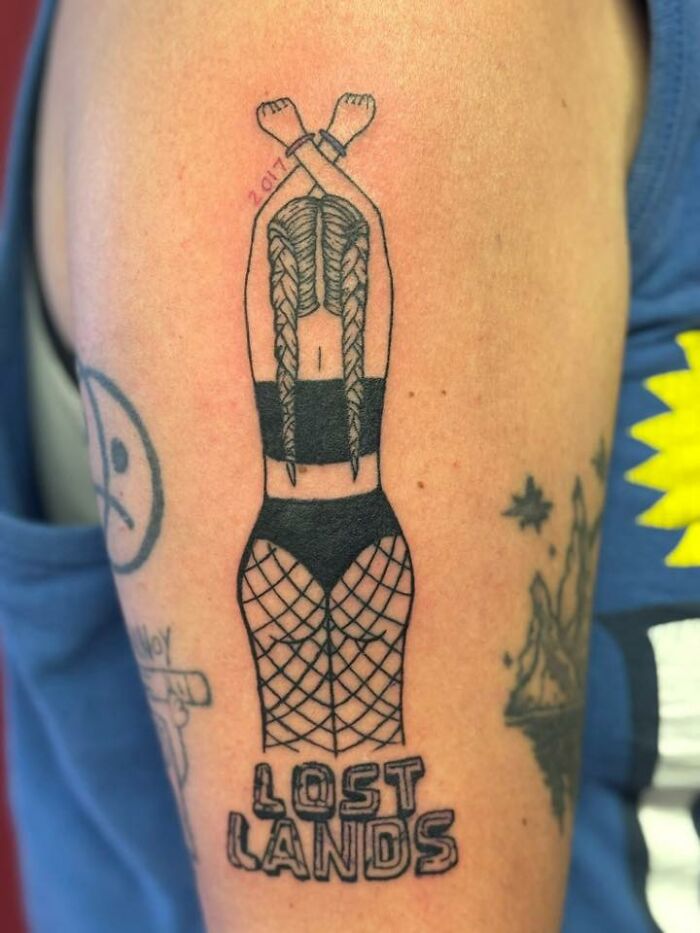 Tattoo of a woman with crossed arms and fishnet stockings with the text Lost Lands, an example of a bad tattoo.