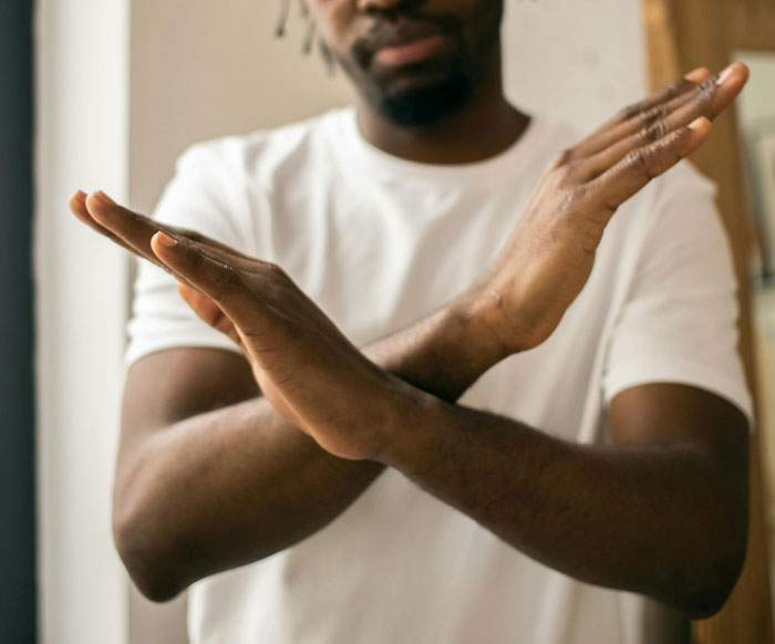 Man in white shirt crossing arms in an X gesture, symbolizing toxic dating trends and unhealthy relationship boundaries.