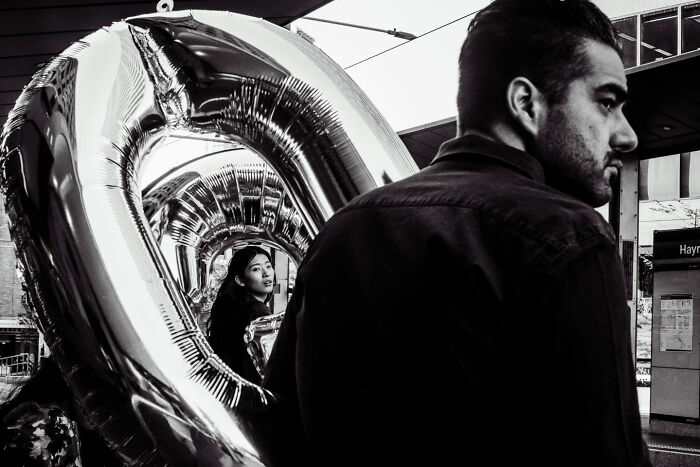 Candid street photo of a man and woman with large reflective balloons, capturing raw urban moments and unique perspectives.