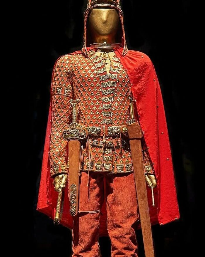 Medieval armor and red cape displayed in a museum showcasing archaeology world historical artifacts and attire.