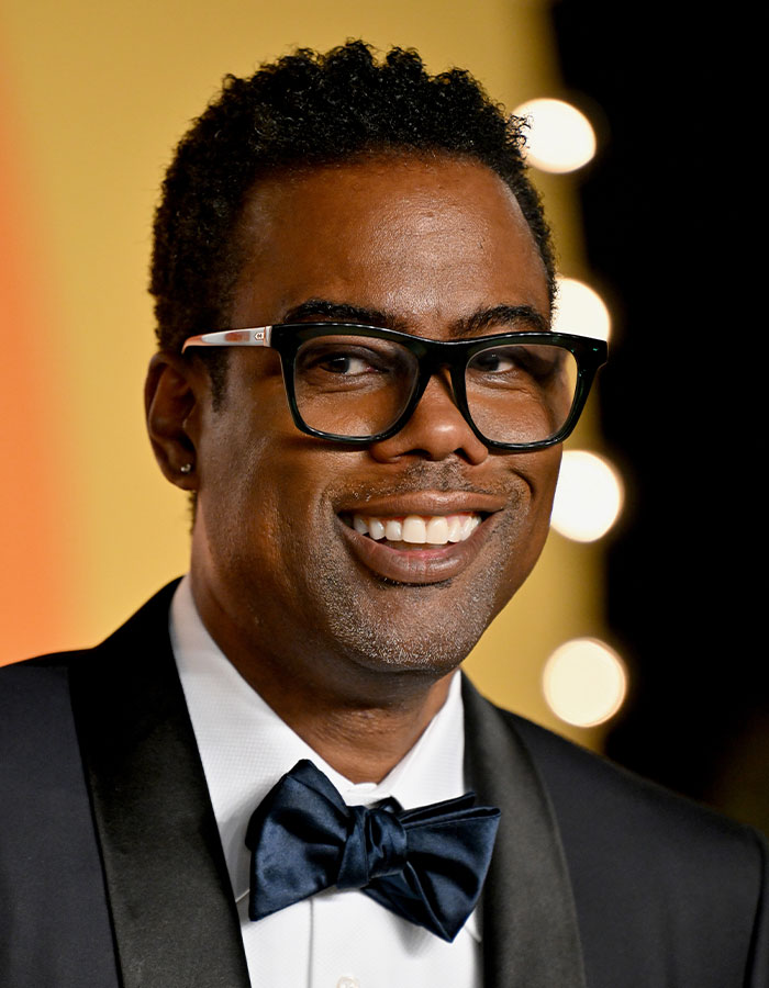 Close-up of a smiling celebrity wearing glasses and a tuxedo, showcasing celebrities who look way younger than they actually are.