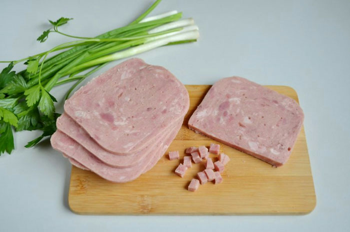 Sliced ham and diced cubes on a wooden board with fresh green onions and parsley, illustrating therapy revelations concept.