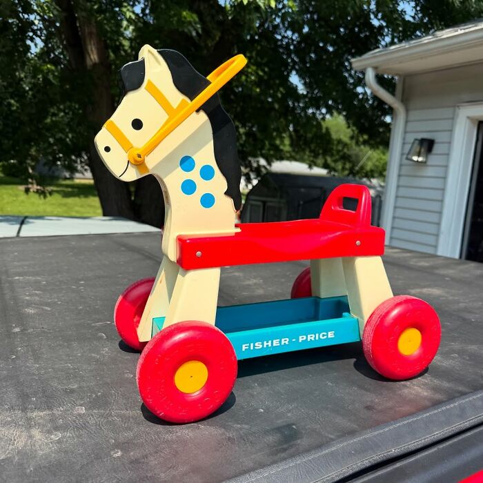 Vintage Fisher Price wooden horse toy with red wheels, a cool secondhand find displayed outdoors on a sunny day.