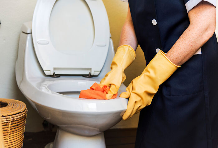 Person wearing yellow gloves cleaning a toilet, illustrating professions people think attract the most awful people. - 25
