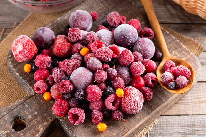 Assorted frozen berries on a wooden board with a spoon, illustrating best processed foods for weight loss.