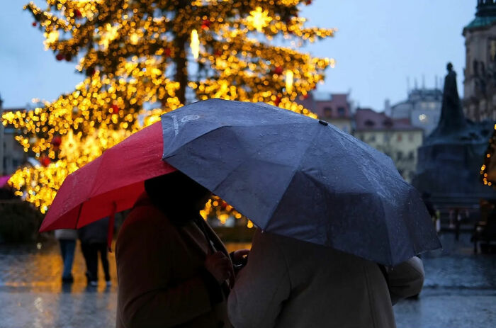 Two people with umbrellas standing in a rainy street scene, capturing the beauty of everyday life in a city.