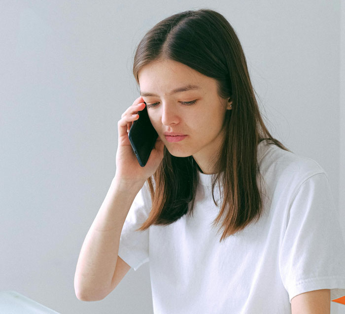 Young woman in a white shirt looking concerned while speaking on a smartphone, reflecting on biggest mistake experiences.